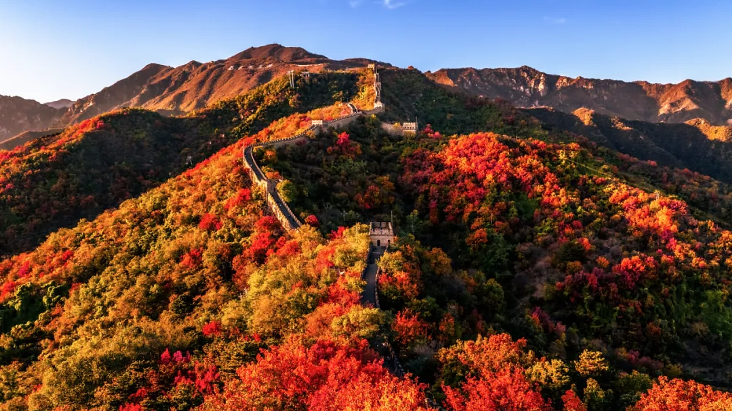 The Great Wall at Mutianyu in autumn, winding through red and orange foliage on the surrounding mountains