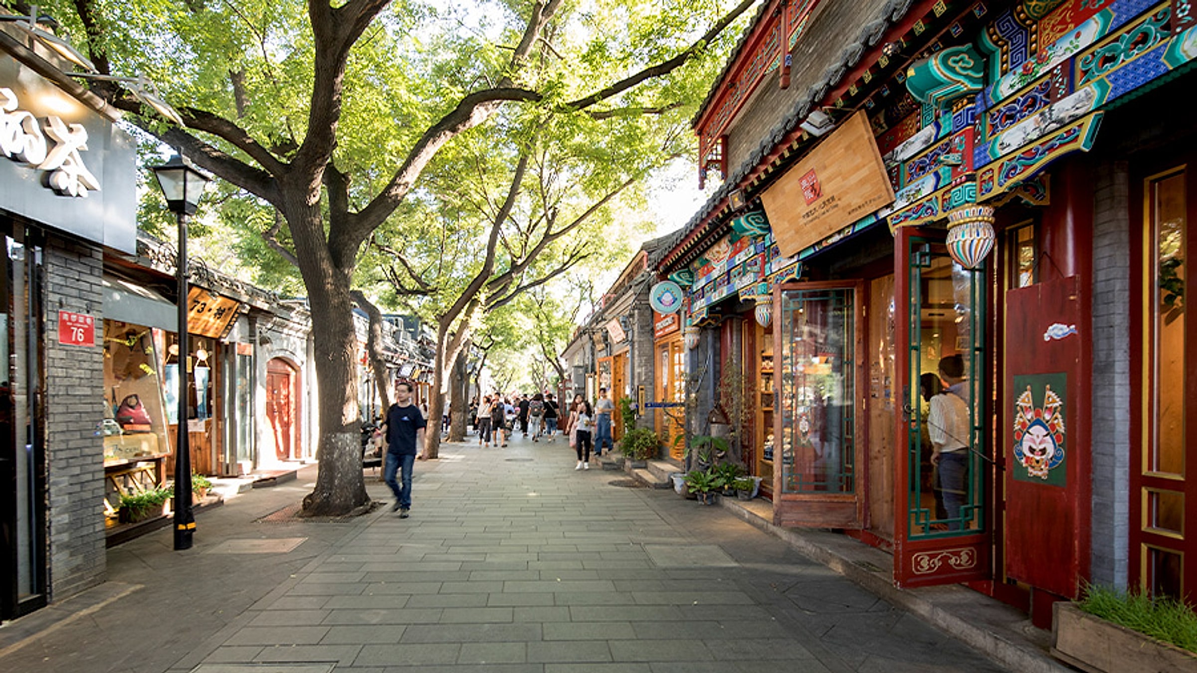 Nanluoguxiang hutong pedestrian street with traditional courtyard houses and painted shopfronts under green trees