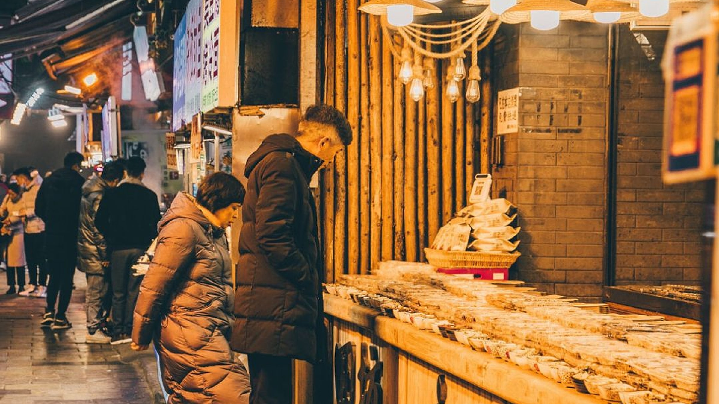 Muslim Quarter night market with warm lantern lighting, a couple browsing a stall, and Chinese signage overhead