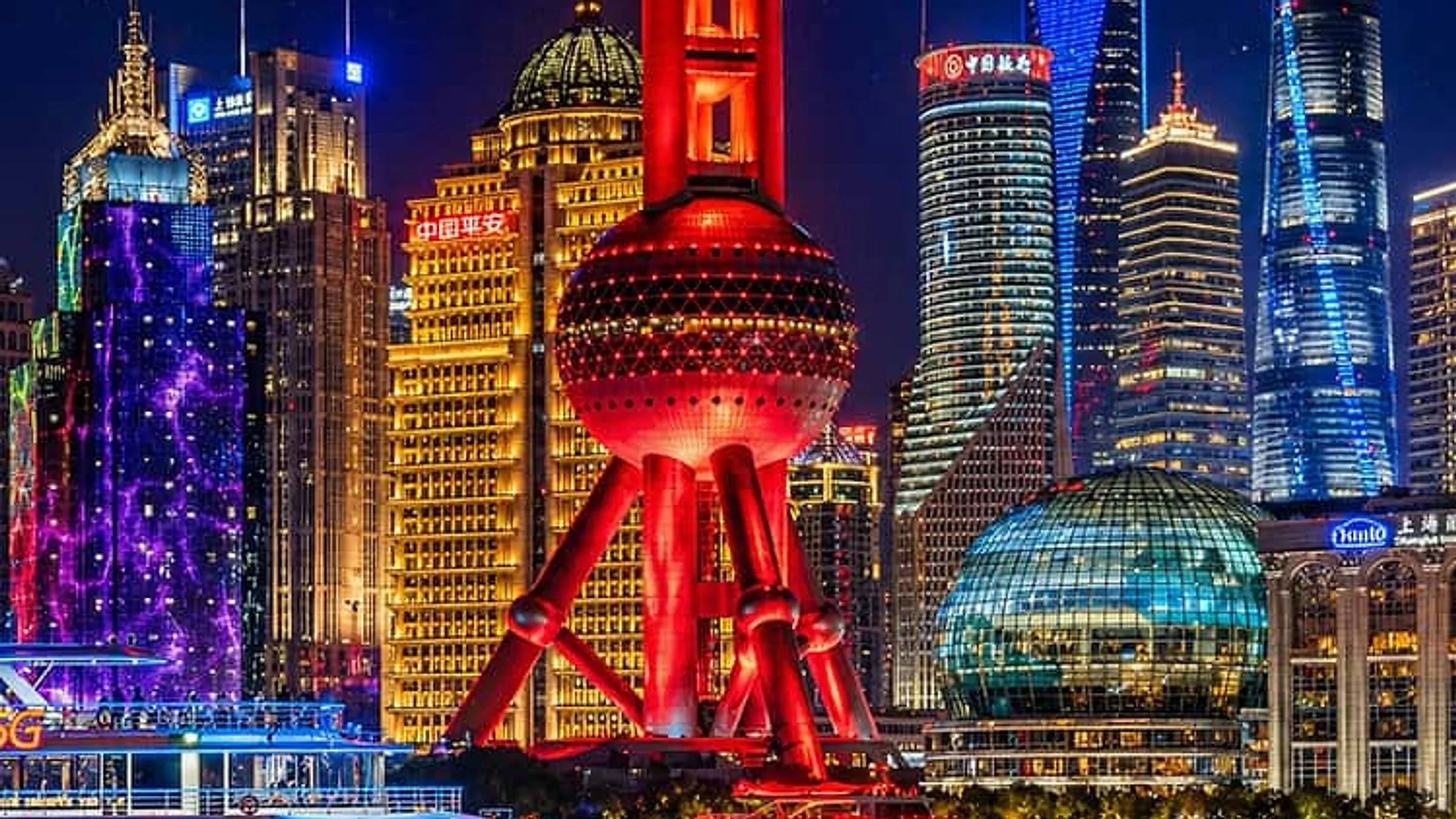 The Bund at night with the red Oriental Pearl Tower, modern Pudong skyscrapers, and a cruise boat on the Huangpu River