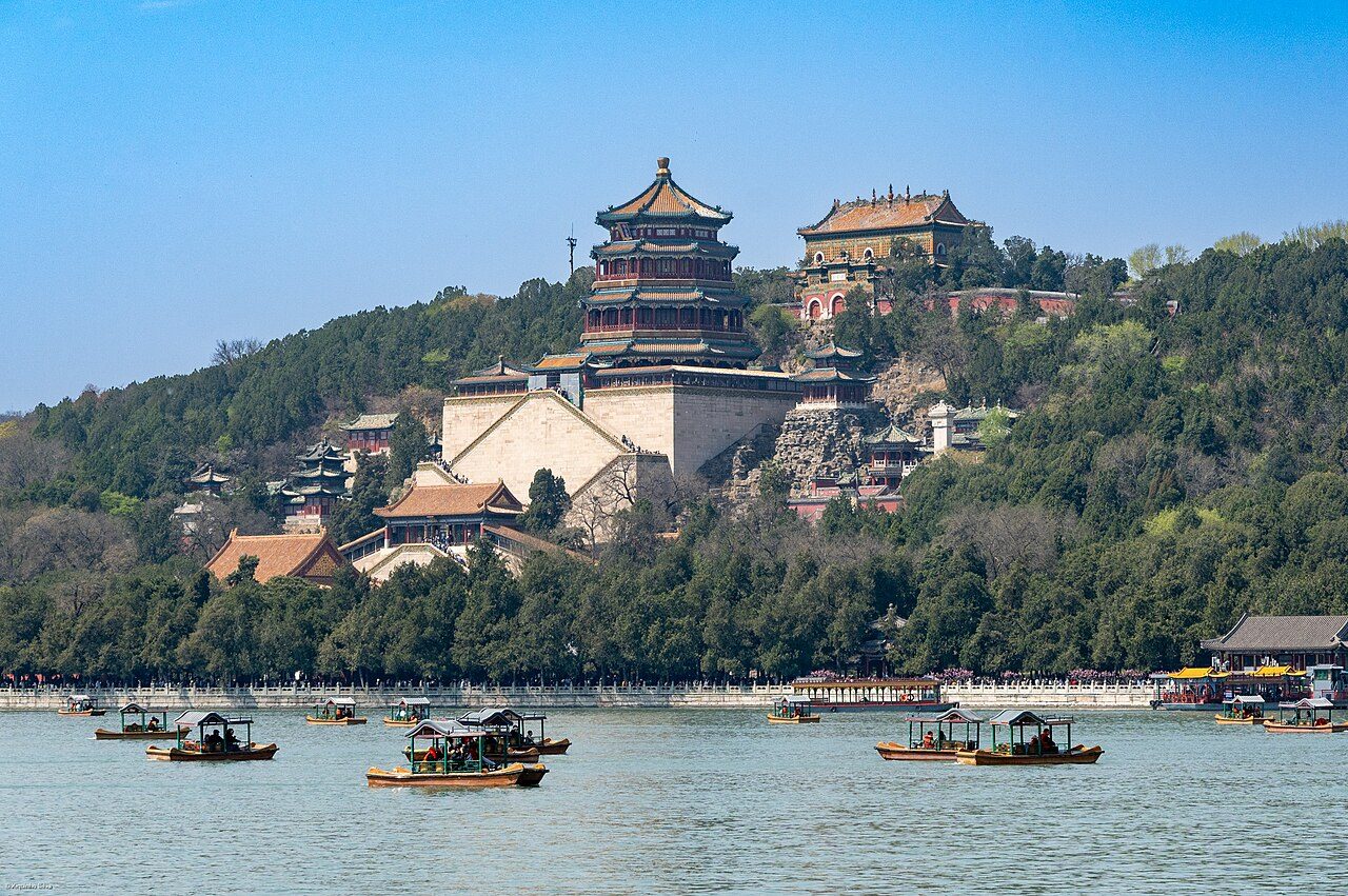 Aerial view of Kunming Lake at the Summer Palace, with traditional Chinese pavilions along the shore and the modern Beijing skyline in the background