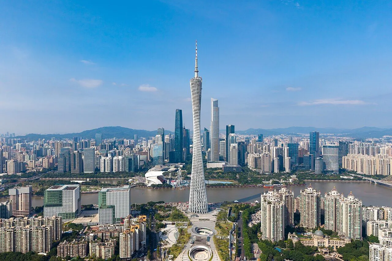 Aerial view of Canton Tower in Guangzhou — the 600-meter hyperboloid TV tower on the south bank of the Pearl River, with the Zhujiang New Town CBD skyline behind it and the Haixinsha Park and Opera House at its base