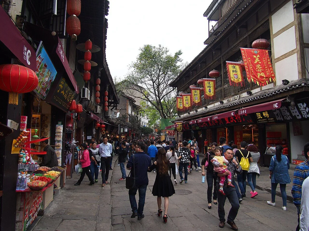 Crowded main street of Ciqikou Ancient Town in Chongqing, lined with Ming-Qing shopfronts, red lanterns, and hundreds of visitors walking past street-food stalls and traditional banners