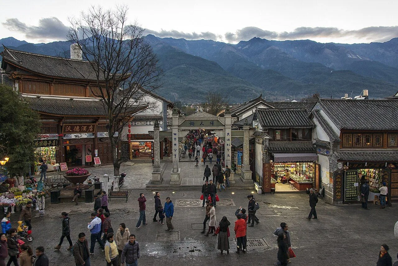 Renmin Lu central plaza in Dali Old Town — the central square of the ancient walled town, with the 5th century Renmin Lu stone arch, locals walking, the Cangshan mountains rising in the background