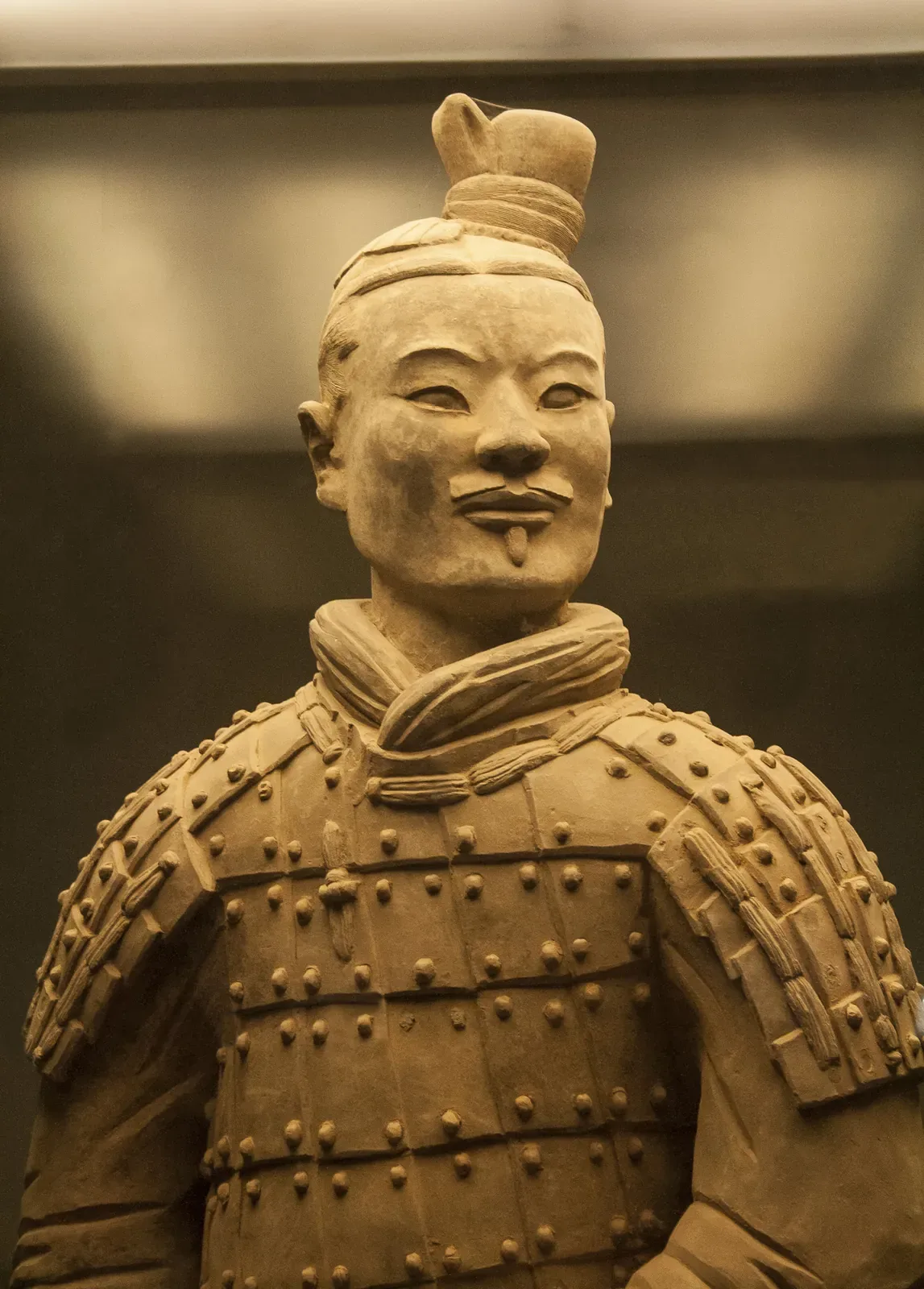 Close-up of a single terracotta general warrior in Pit 1, showing the detailed armor plates, topknot hairstyle, and the slight turn of the head — a single figure from the army of more than 8,000