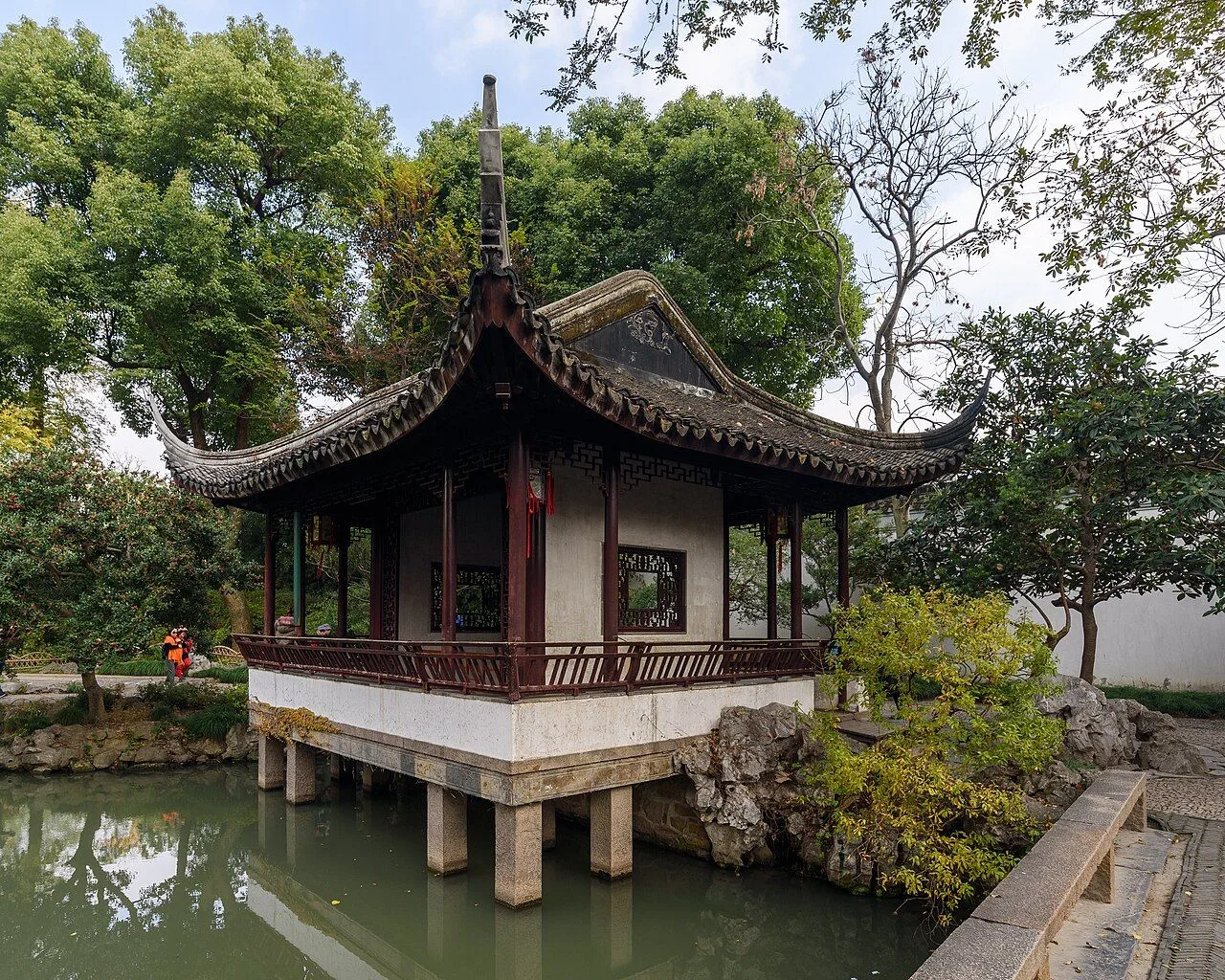 The classic Humble Administrator's Garden pavilion in Suzhou — a traditional Chinese wooden pavilion on a stone base above the pond, with upturned eaves and autumn trees, the largest classical garden in Suzhou (5.2 hectares) and a UNESCO World Heritage Site since 1997