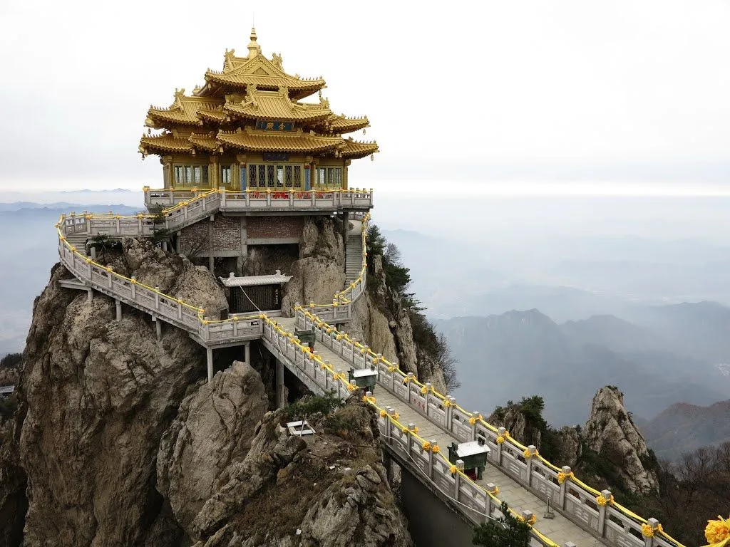 The Điện Linh Quan (灵官殿) golden-roofed Taoist temple perched on a knife-edge cliff at the summit of Laojun Mountain (老君山) in Luanchuan County, Henan — the signature visual of the mountain, with stone walkways and railings connecting the building to the granite ridge and the misty valleys below