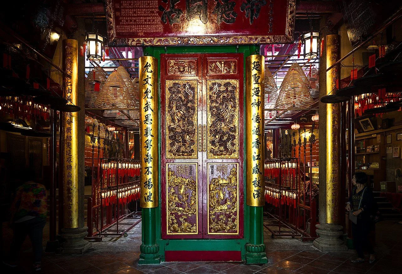 The ornate entrance to the Man Mo Temple in Sheung Wan, Hong Kong — golden carved doors flanked by massive pillars with Chinese inscriptions honoring the gods of literature (Man Cheong / 文昌) and martial arts (Mo Tai / 武帝), built in 1847 during the Qing dynasty. The temple is a declared Grade I historic building