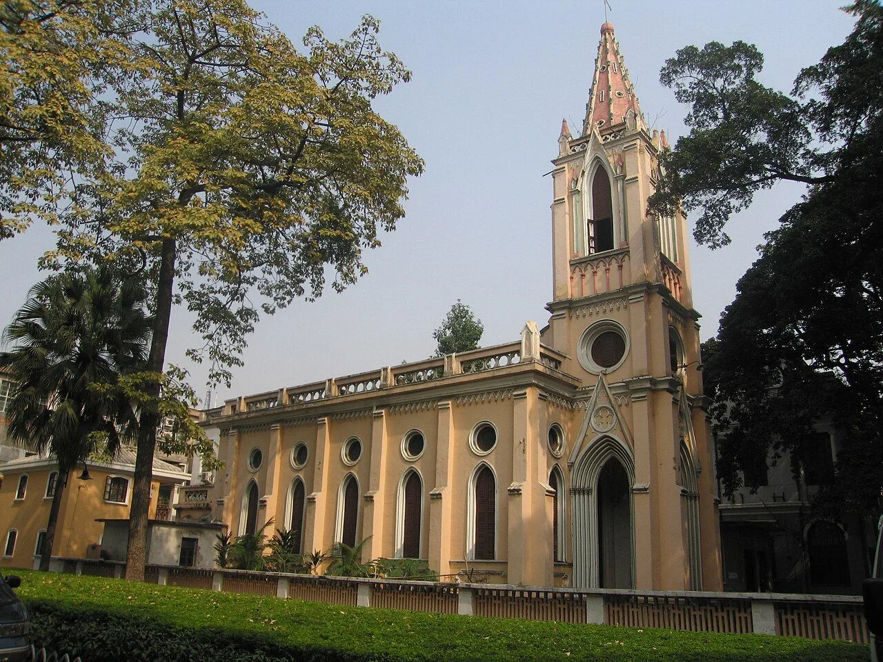 The Our Lady of Lourdes Chapel on Shamian Island, Guangzhou, a 1892 Gothic Revival Catholic church with a tall pointed spire and arched stained-glass windows along the side, framed by tropical trees on the island
