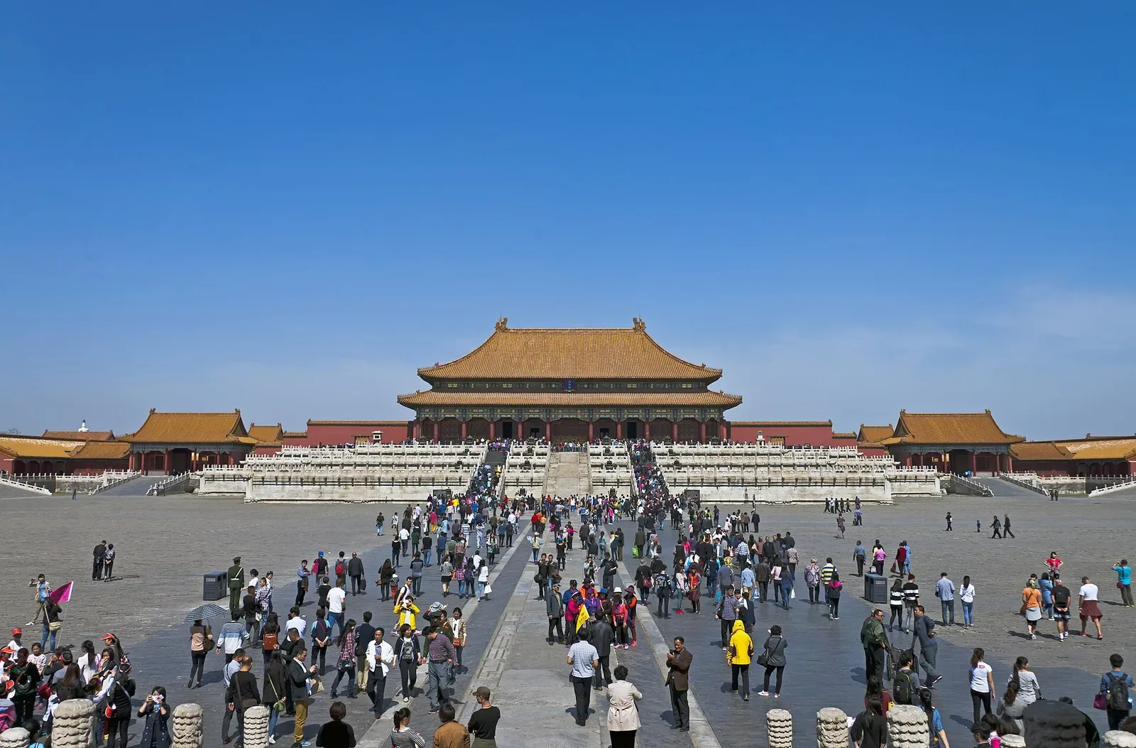 The Hall of Supreme Harmony at the Forbidden City, Beijing — the largest wooden hall in the complex, golden roof tiles and red walls, with the central stone-paved courtyard and a crowd of visitors walking toward the entrance on a clear day