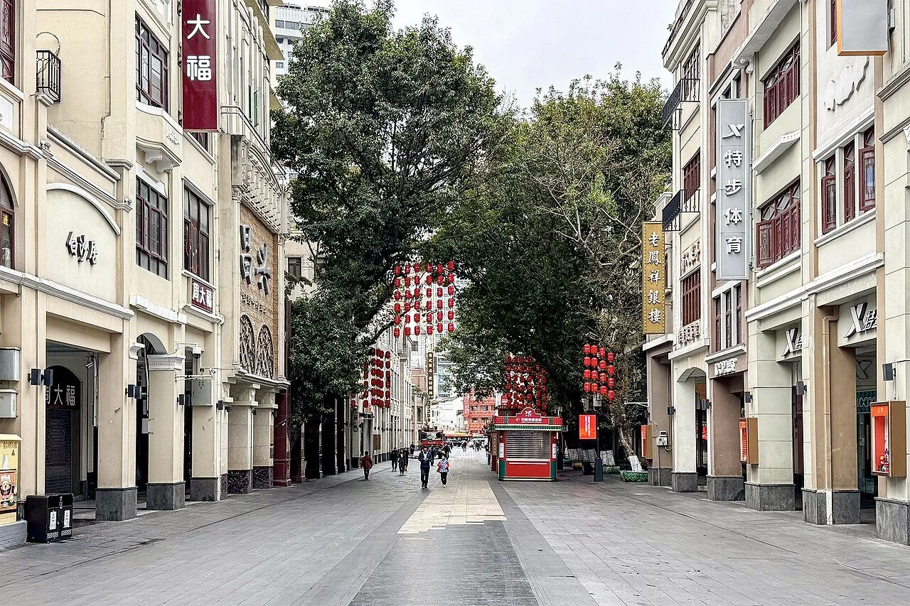 Beijing Road pedestrian street on a quieter day, looking down the 1930s arcade buildings with rows of red lanterns strung between the buildings and Chinese flags flying above the storefronts