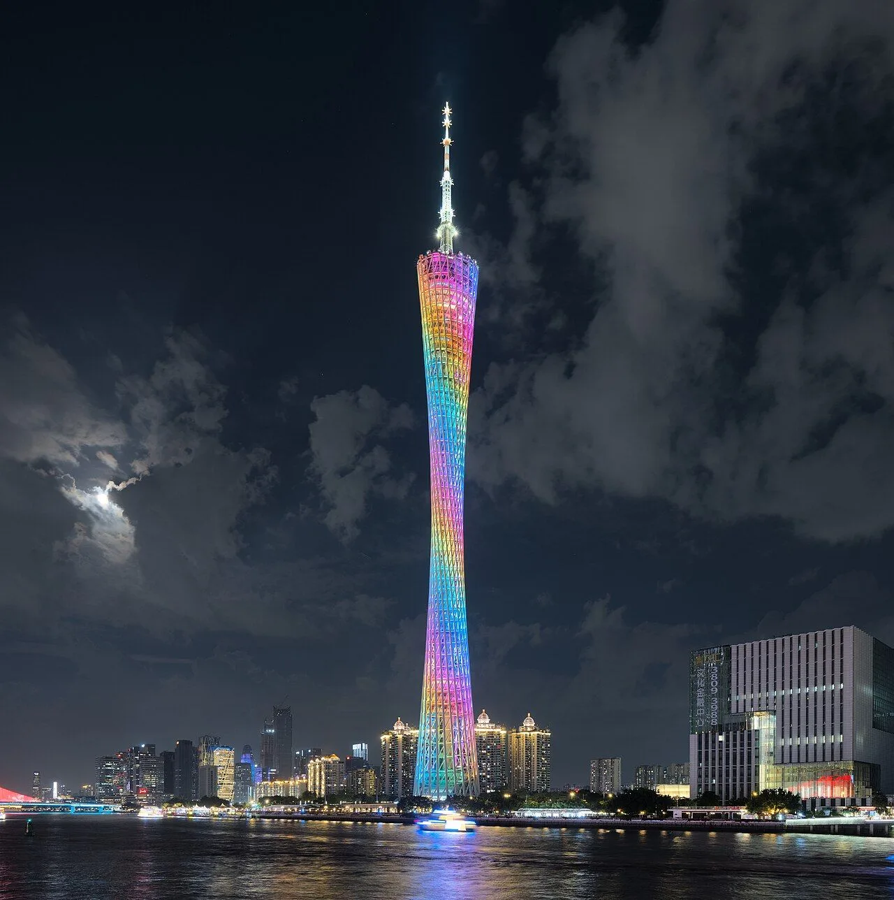 Canton Tower in Guangzhou lit up at night in rainbow LED colors, viewed from across the Pearl River with the boats and the Haizhu skyline in the foreground — the iconic 4,500-LED nightly light show