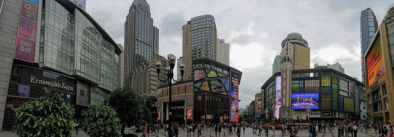 The Jiefangbei Pedestrian Street w/ shopping crowds, GUCCI, Ermenegildo Zegna, Miu Miu storefronts, and the Chongqing skyscrapers — the heart of the CBD and the most-visited street in Chongqing with 1.6 million people daily on weekends
