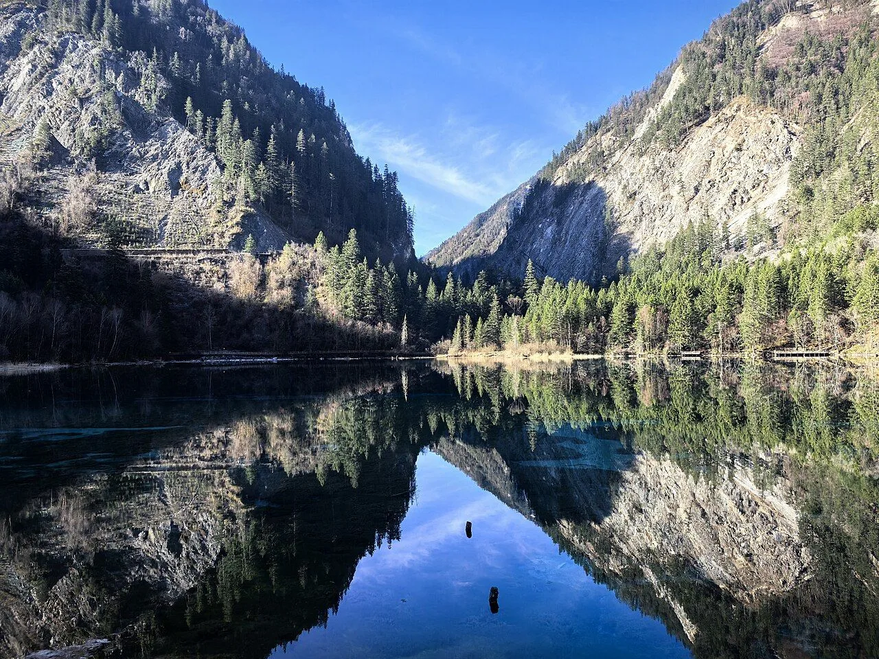 A mirror-reflection lake in Jiuzhaigou Valley with the surrounding peaks, forests, and blue sky all perfectly reflected in the calm water — a UNESCO World Heritage Site, the valley stretches 80 km through the Min Mountains on the edge of the Tibetan Plateau