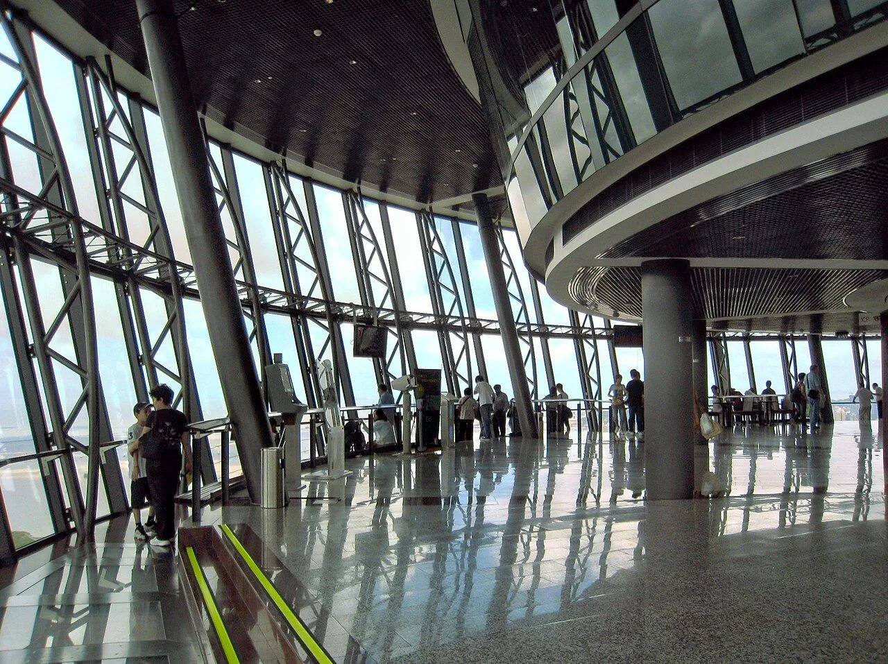 The 360° Café observation deck inside Macau Tower — floor-to-ceiling glass walls wrap the entire level, with visitors looking out over the Pearl River Delta and the 233m-high Skywalk X observation platform visible at the edge. The tower has 17 observation and entertainment levels