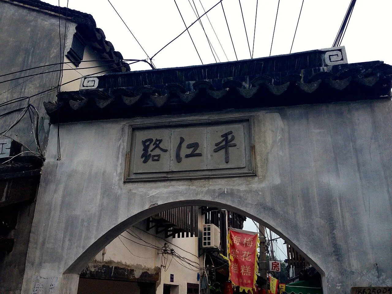 The historic stone gate of Pingjiang Road (平江路) in Suzhou — a whitewashed brick archway with the characters 平江路 (Pingjiang Lu) carved into a stone plaque, the entrance to one of the best-preserved old streets in the Yangtze Delta, dating back to the Song dynasty (960-1279) and laid out on the same plan as the 11th-century Pingjiang Map
