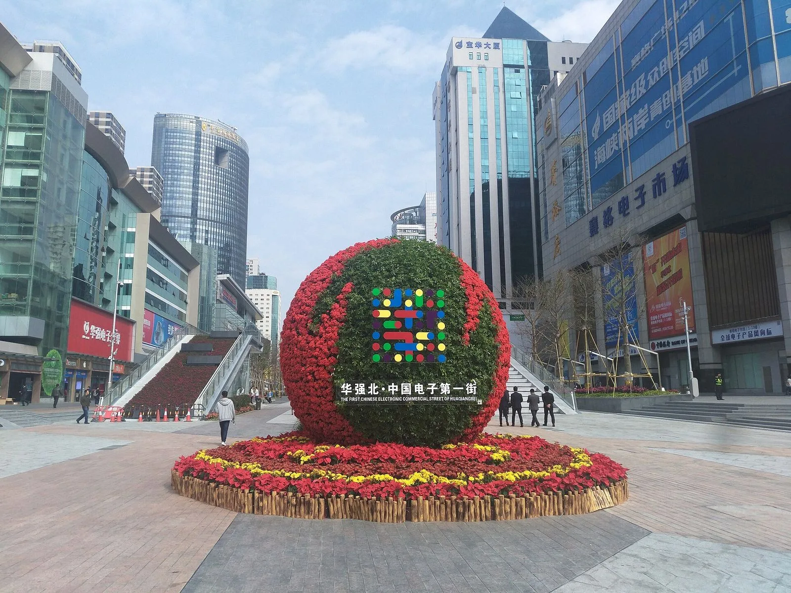 The Huaqiangbei plaza at the heart of the district, with the iconic red "华强北 中国电子第一街" (Huaqiangbei, China's No.1 Electronics Street) floral sculpture in the foreground and the SEG Plaza tower and surrounding electronics malls rising behind