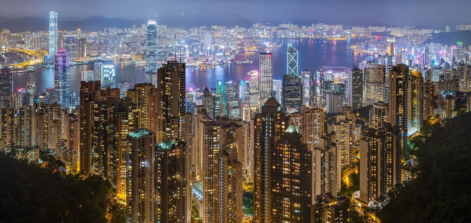 The night skyline of Hong Kong Island and Victoria Harbour viewed from Victoria Peak — the dense cluster of illuminated skyscrapers on Hong Kong Island with the harbour water below, the world-famous view that has been called the greatest night view in the world and inspired the Symphony of Lights show every night at 8pm, the scene visible from Sky Terrace 428 and the Peak Tower observation deck