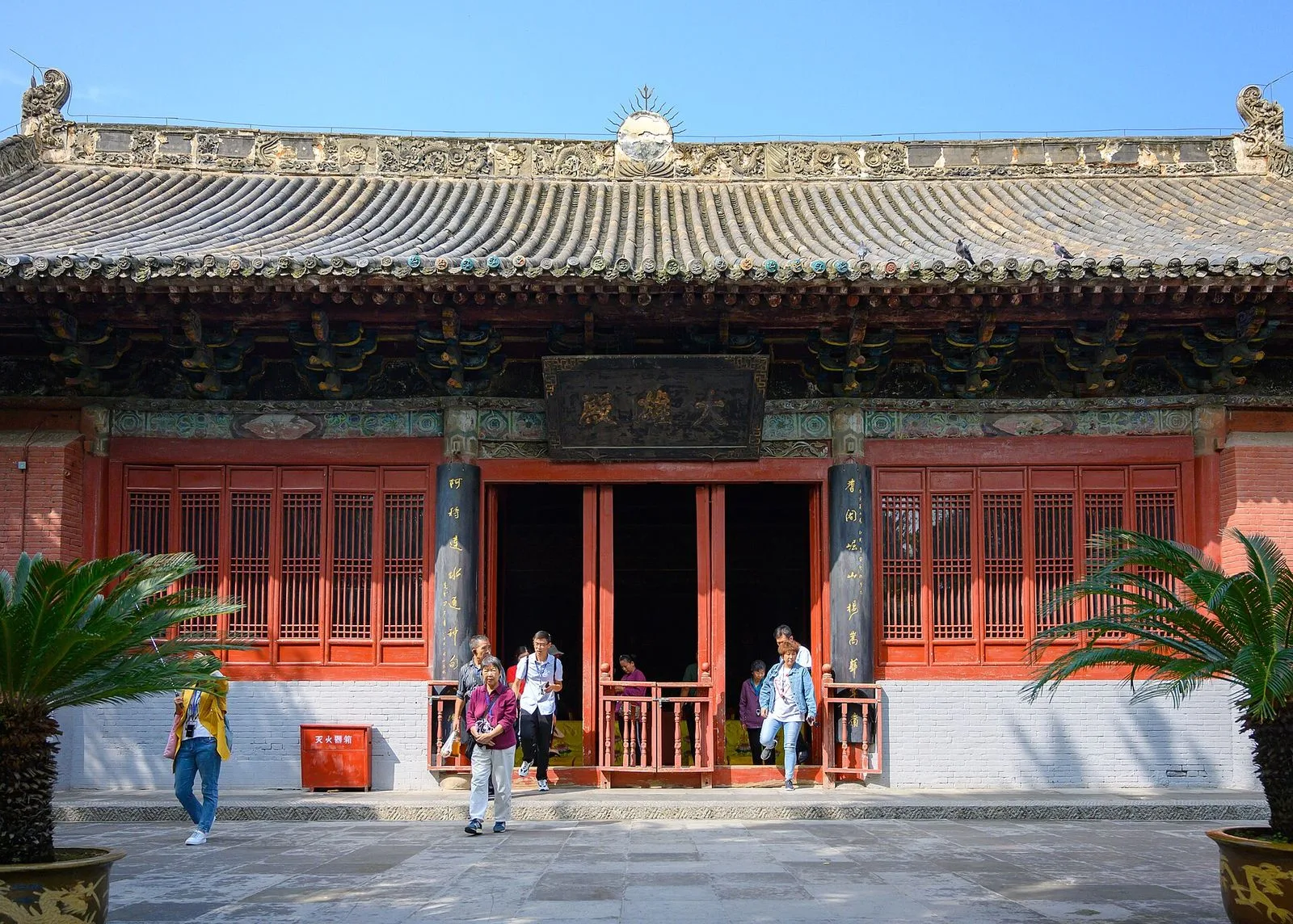 The Great Buddha Hall (大佛殿) of the White Horse Temple in Luoyang — the Chinese-style wooden temple hall with the distinctive upturned eaves and the elaborate painted dougong brackets, the visitors walking through the central doors, the sun emblem on the roof ridge, the main hall of the 1900-year-old temple where the Sakyamuni Buddha is enshrined and the monks perform the morning chanting ceremony every day at 4:30am