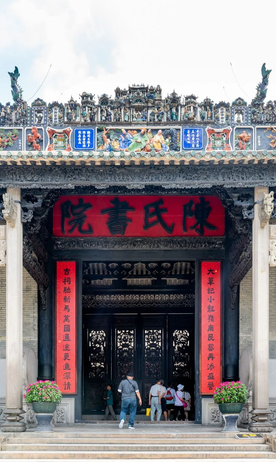 Vertical close-up of the Chen Clan Ancestral Hall entrance in Guangzhou, showing the 陳氏書院 red signboard, the ceramic-figure covered pediment, and visitors climbing the steps — the showcase of Lingnan ancestral-hall decoration