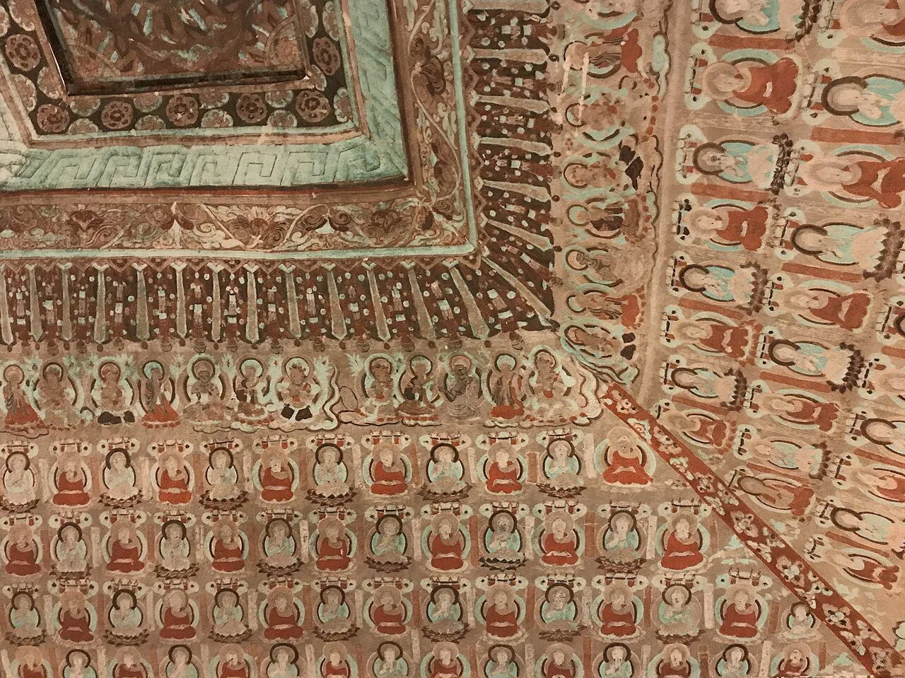 Mogao Cave 220 (early Tang dynasty, 642 AD) — rows of small painted Buddha figures seated in their own alcoves, with the ornamental coffered ceiling and the central pillar of the prayer hall — a UNESCO masterpiece