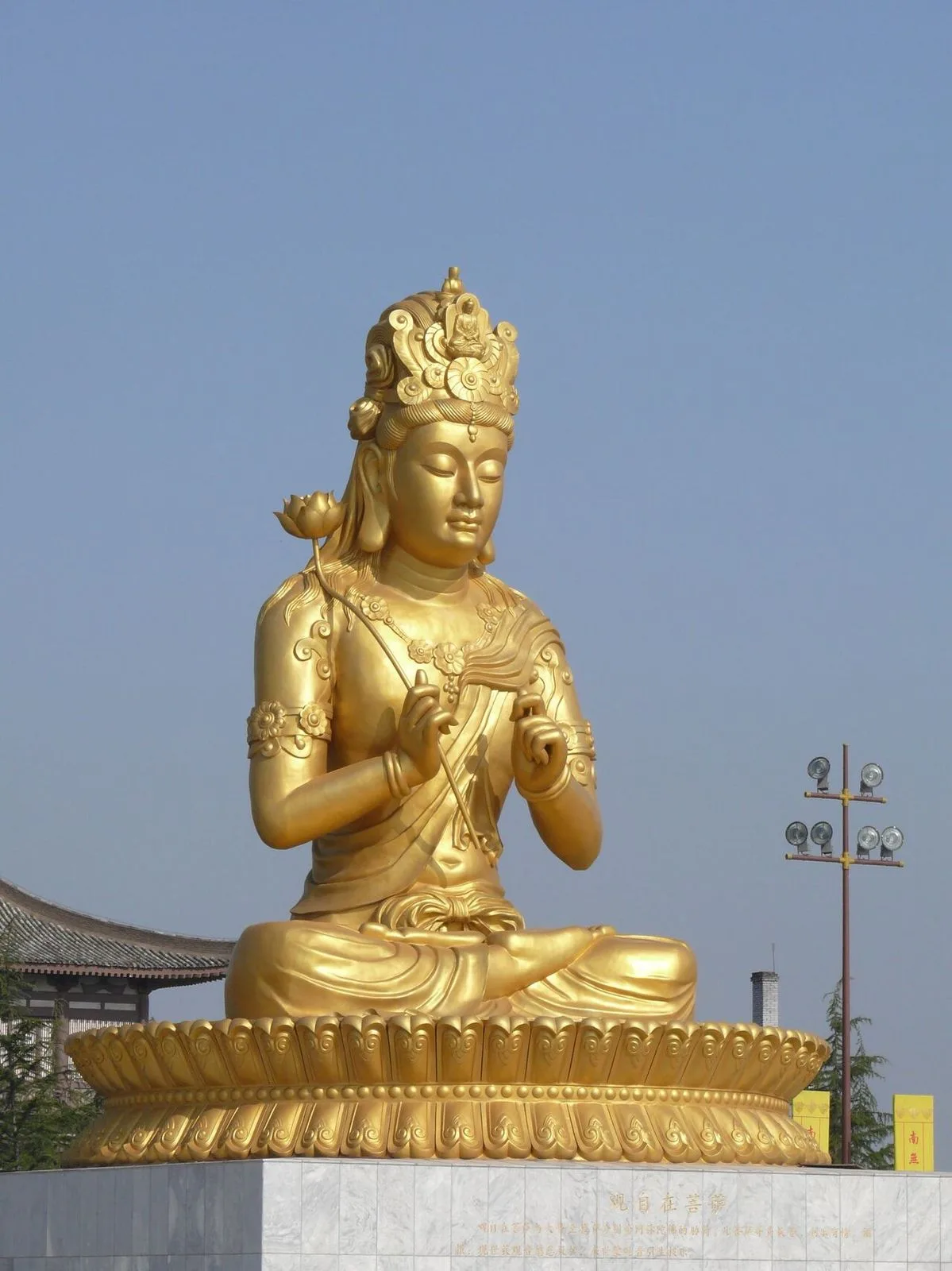 The large golden Guanyin (Bodhisattva) statue at Famen Temple, shown in close-up with the right hand raised in the Abhaya mudra (gesture of fearlessness) against a clean blue sky, the gold surfaces reflecting the bright sunlight