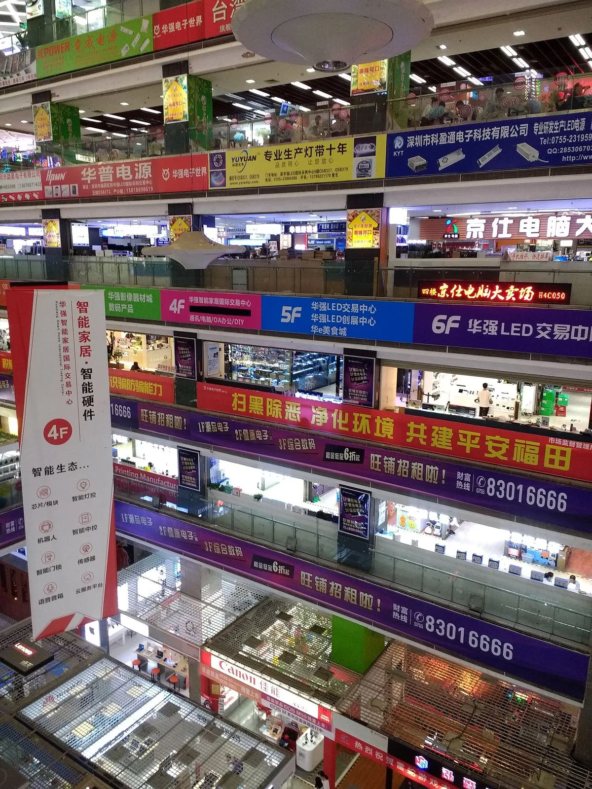 Inside the multi-floor Huaqiang Electronics World — the interior of one of the 30+ electronics malls in Huaqiang North, with neon signs, multi-level walkways, and shops selling components, phones, and consumer electronics visible across at least four floors