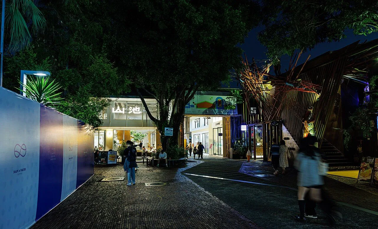OCT LOFT at night — the pedestrian cobblestone street lined with creative shops, gallery spaces, and design studios, lit by string lights and lanterns, the popular evening hangout for Shenzhen creatives and visitors. The complex hosts 50+ art spaces and 100+ creative companies