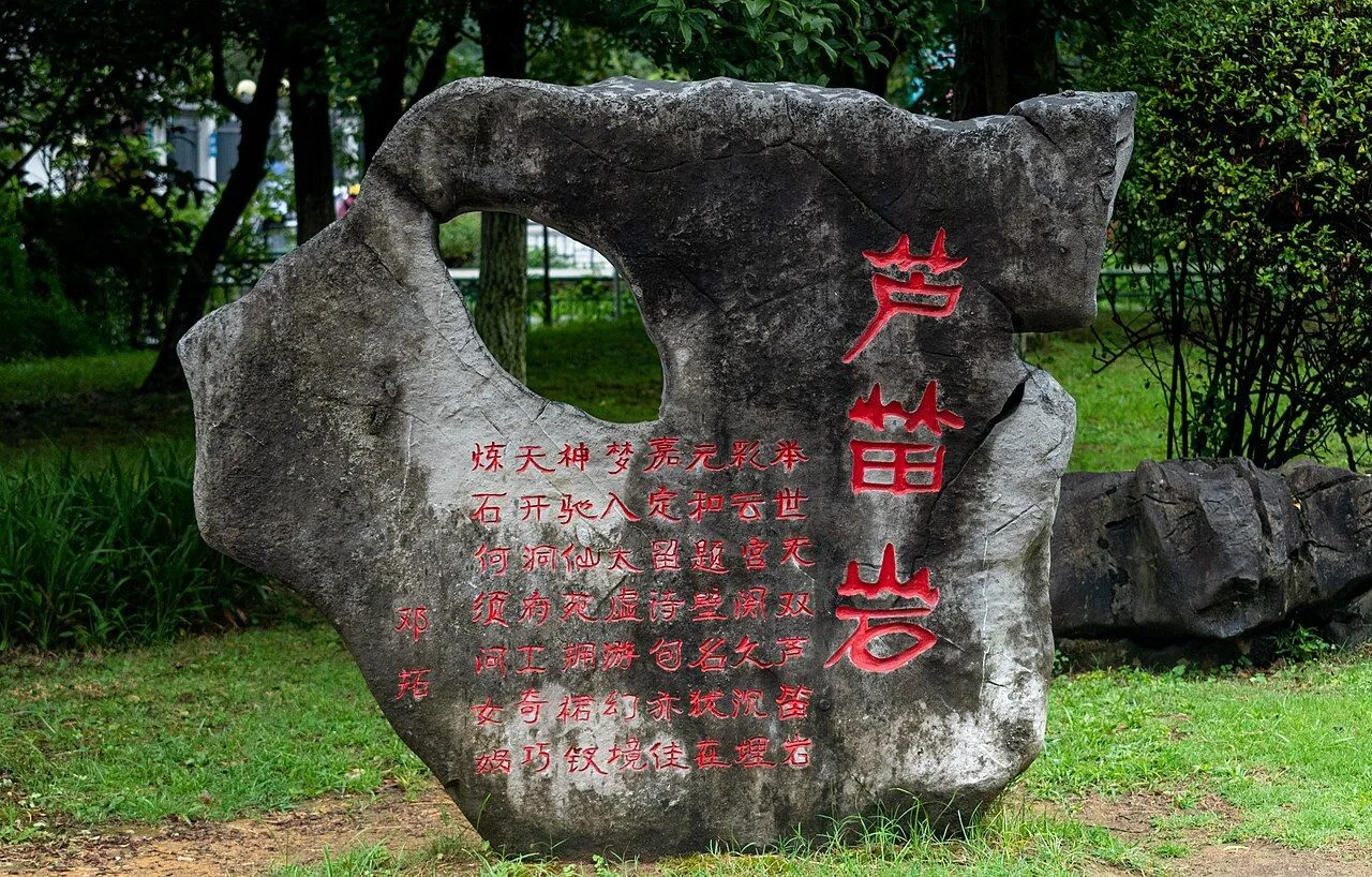 The entrance stone of Reed Flute Cave (芦笛岩) — a 2m-tall weathered limestone boulder engraved with the three red characters 芦笛岩 (Ludi Yan, "Reed Flute Rock") and a poem by the Tang dynasty poet Wang Wei, the calligraphy and entrance garden that introduce visitors to this Guilin landmark that has been a tourist attraction since the Tang dynasty