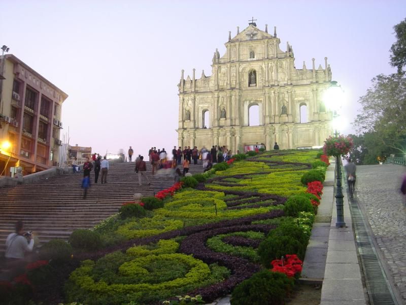 The Ruins of St Paul’s at dusk — the carved Baroque facade lit against the evening sky, with the broad stone staircase and the manicured garden walkway leading up to it, the approach that the 17th-century Jesuit missionaries would have taken when the cathedral was completed in 1640 and served as the center of Catholic missionary work in East Asia