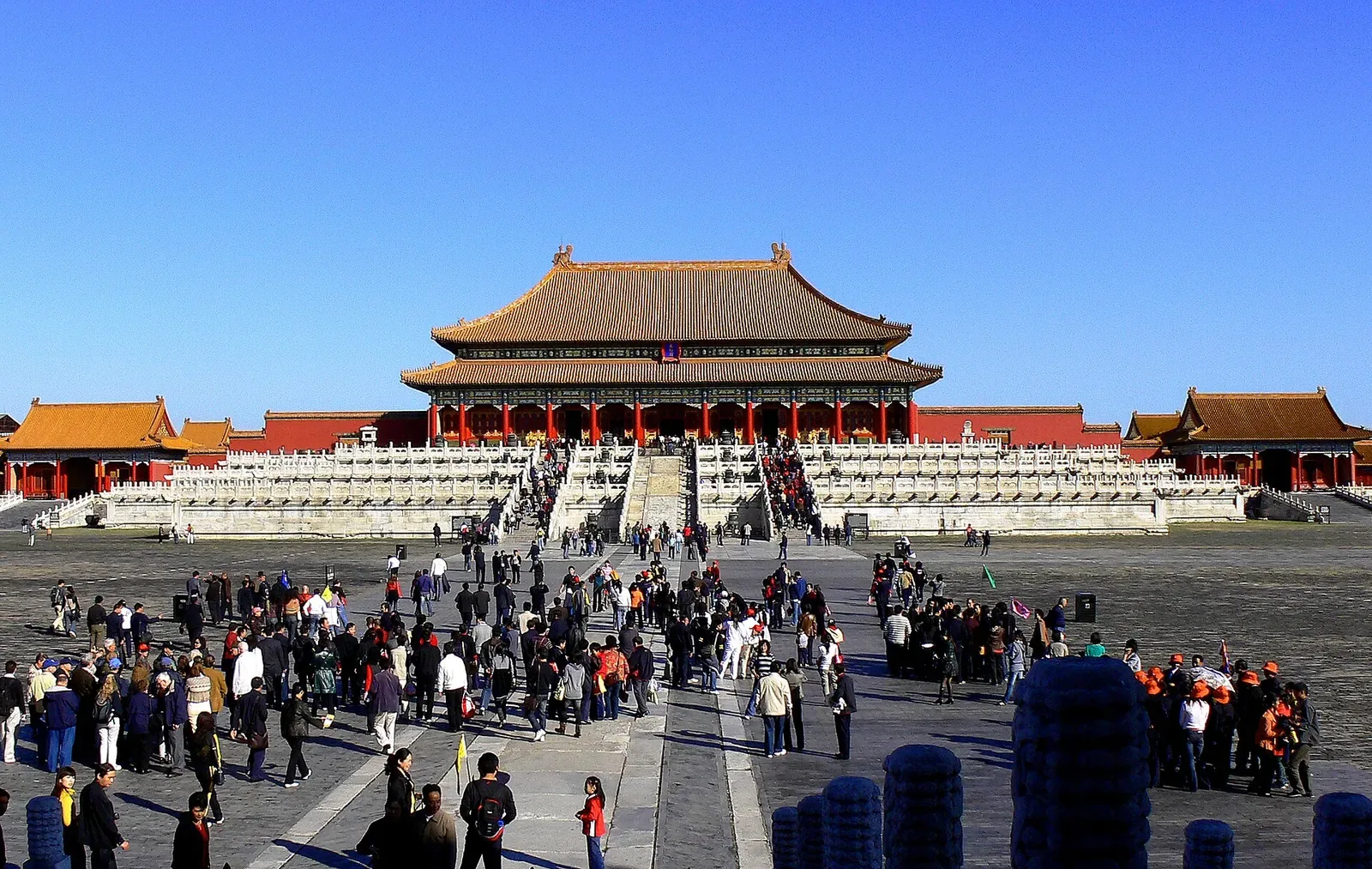 The Hall of Supreme Harmony viewed from the front courtyard at the Forbidden City — three marble staircases, white stone balustrades, and the imposing double-eaved hall with golden roof tiles, photographed from the tourist's approach path on a clear winter day