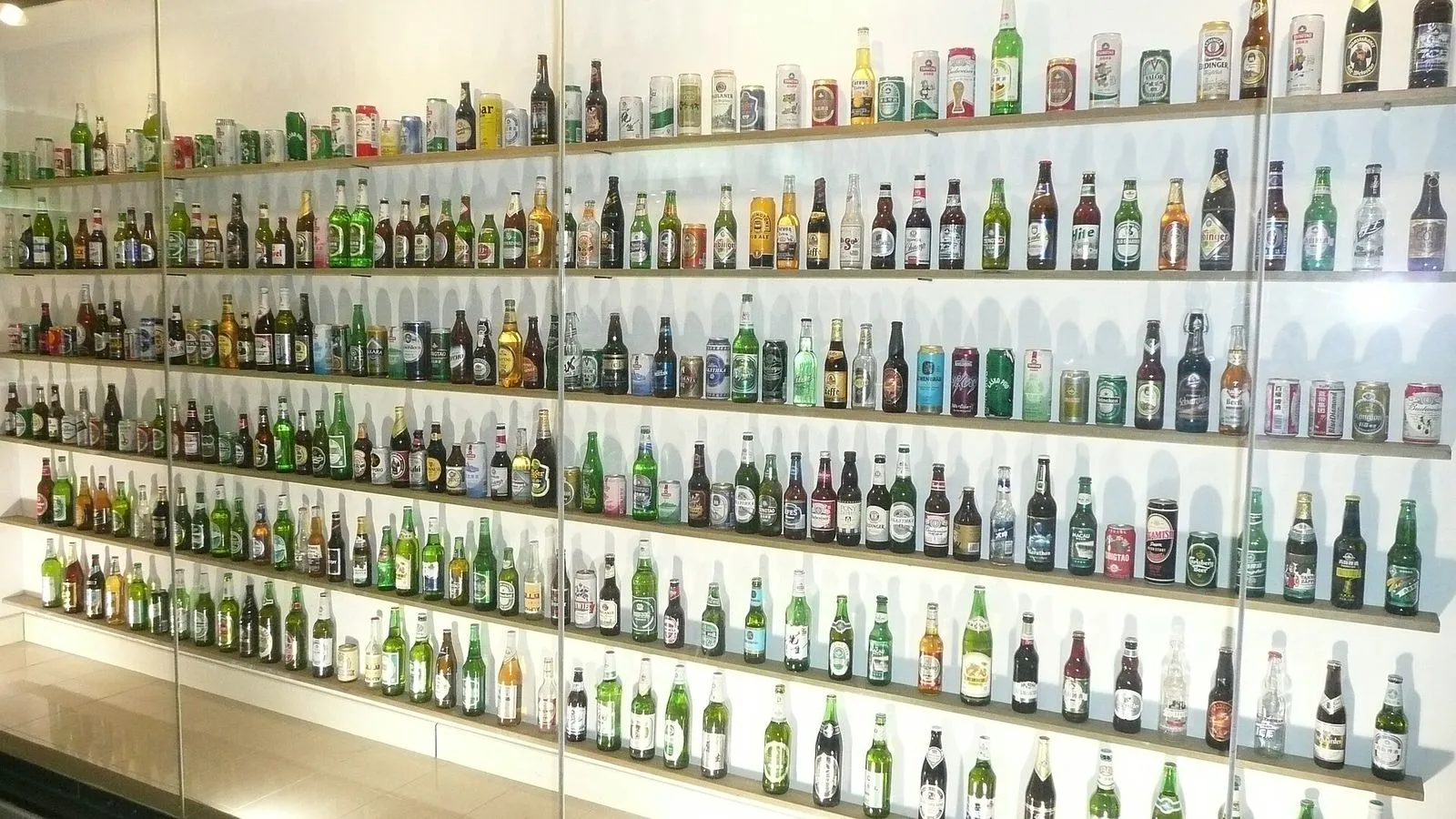 The interior of the Tsingtao Beer Museum showing a wall of vintage Tsingtao beer bottles from different decades — the historical display tracing the 1903 founding by the Anglo-German Brewery Co. through the 1949 nationalization to the present-day Tsingtao Brewery Co. Ltd., the museum exhibits that show the entire brewing process, the original vats and the photo archive of the German founders, the 25 yuan museum ticket that includes a free pint at the end of the tour