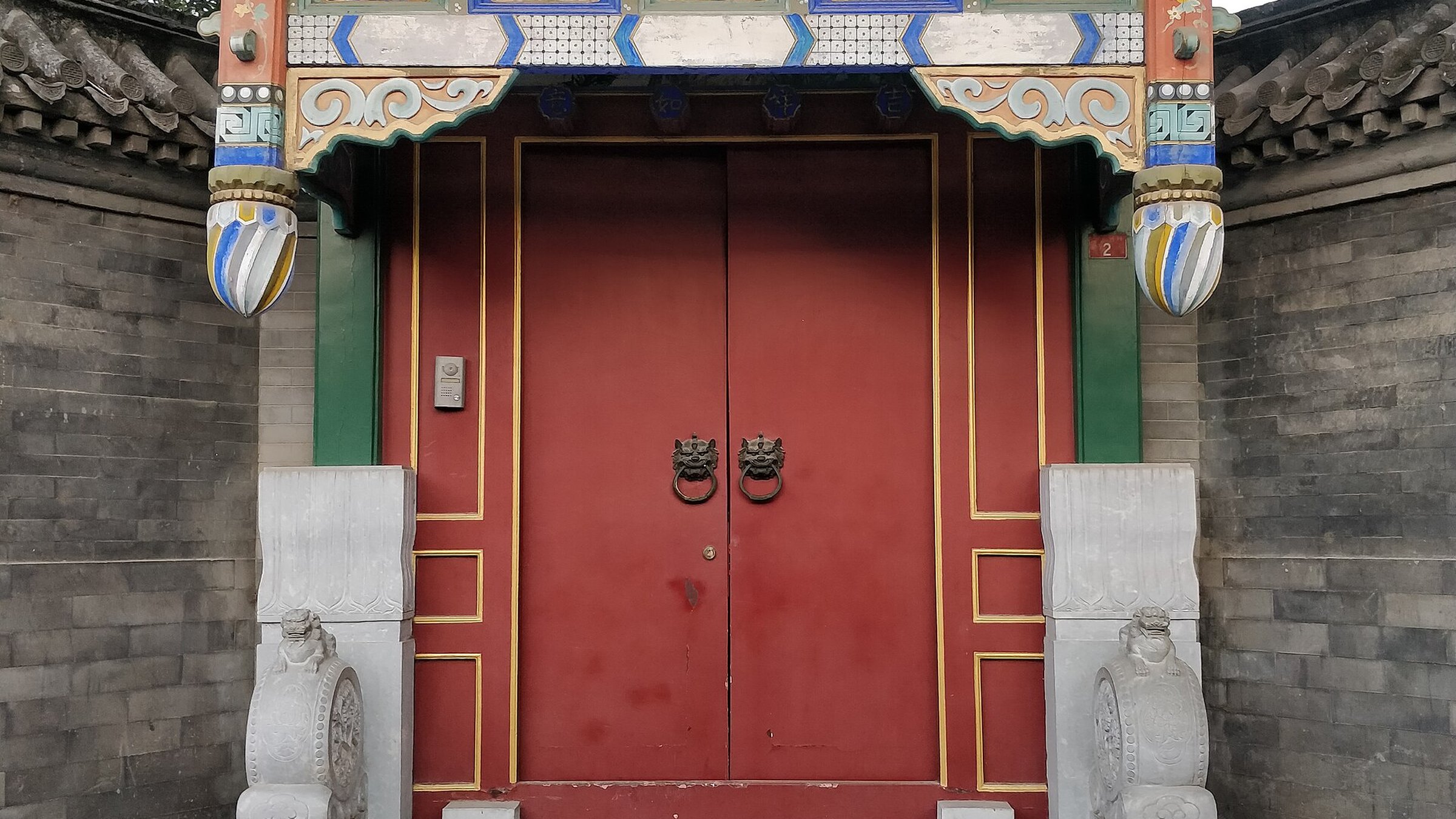 Traditional red door with golden studs and decorative stone base at a Beijing siheyuan courtyard home in a hutong alley