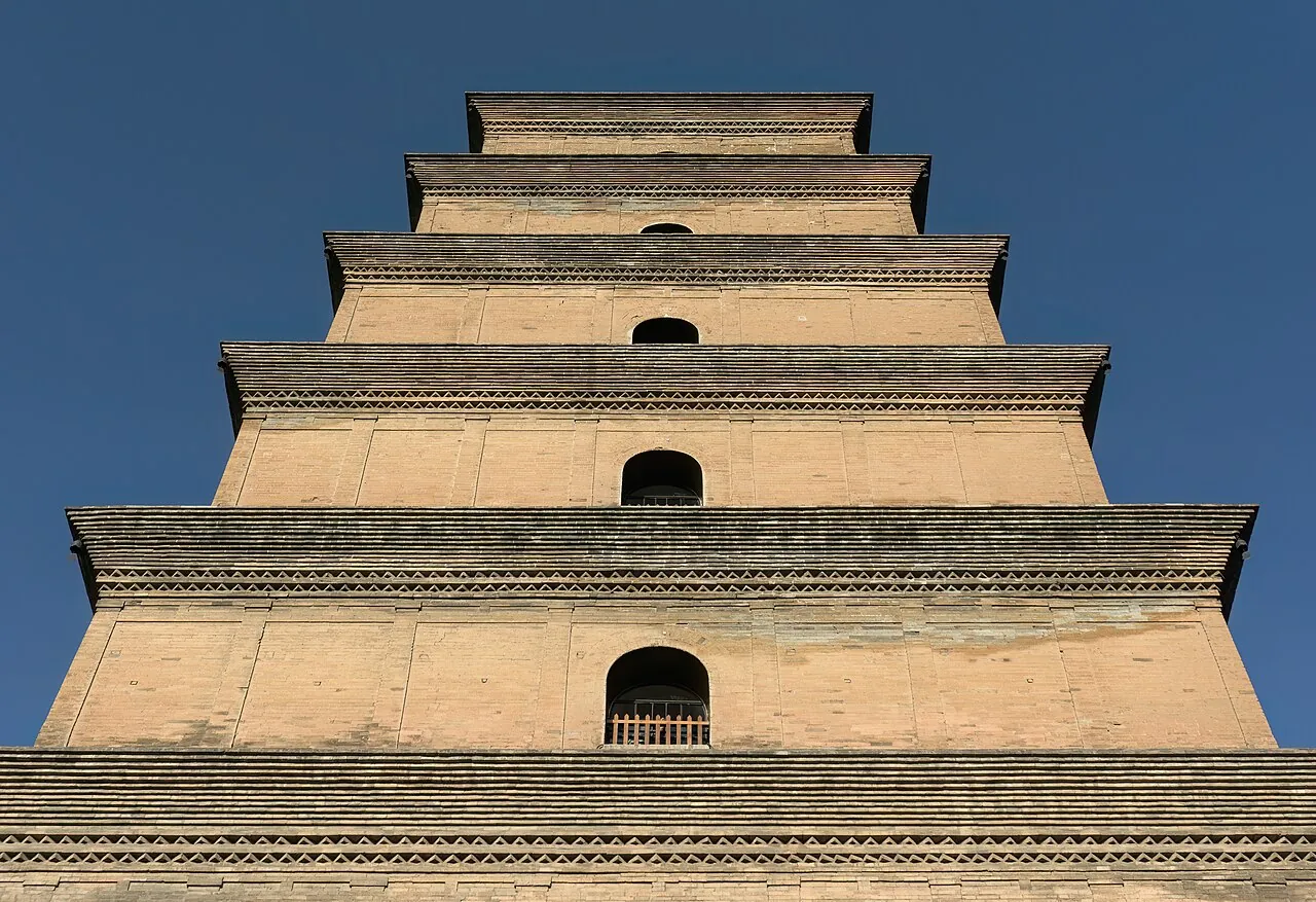 Lantai atas Pagoda Big Wild Goose di Xi'an dengan latar belakang langit biru tua — close-up dari sudut rendah yang menunjukkan 4 lantai atas pagoda bata Dinasti Tang setinggi 64 m, lis batu bata berlapis, bukaan jendela lengkung kecil di setiap tingkat, dan patina halus dari batu bata yang berusia 1.300 tahun — bidikan detail arsitektur pagoda yang paling banyak difoto dan pemandangan yang paling jelas menunjukkan bentuk piramida-persegi era Tang yang membedakan Da Yan Ta dari pagoda Song dan Ming yang bulat kemudian