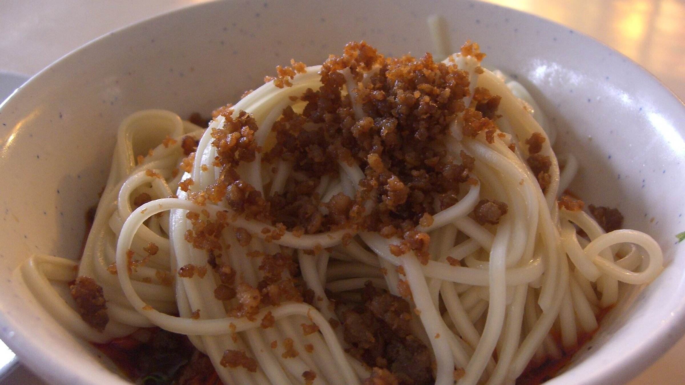 Bowl of authentic Chengdu dan dan noodles with thin wheat noodles topped with spicy minced pork and Sichuan peppercorn