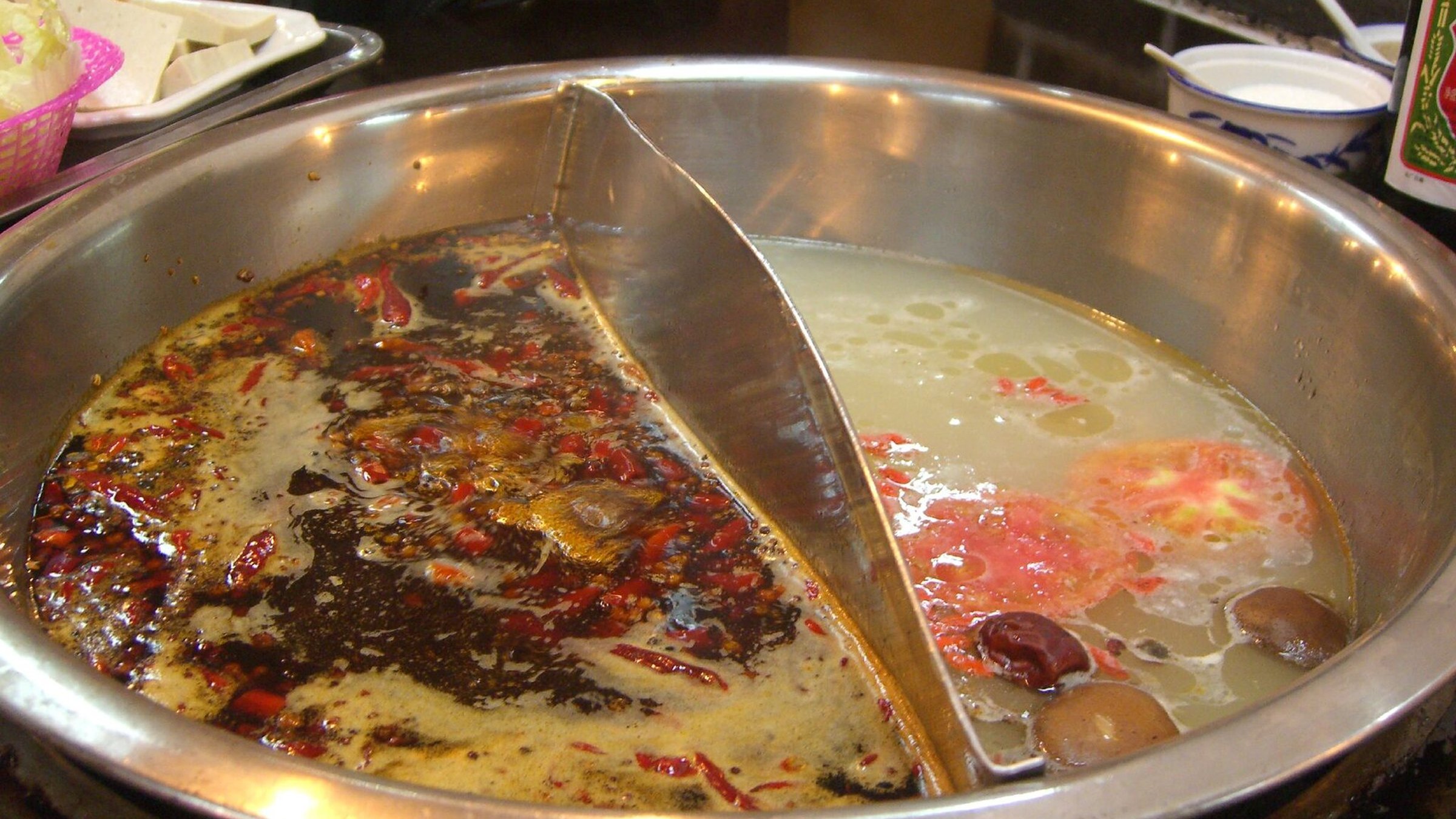 Chengdu-style 鸳鸯 hotpot with red spicy broth on one side and clear bone broth on the other, with ingredients ready to cook