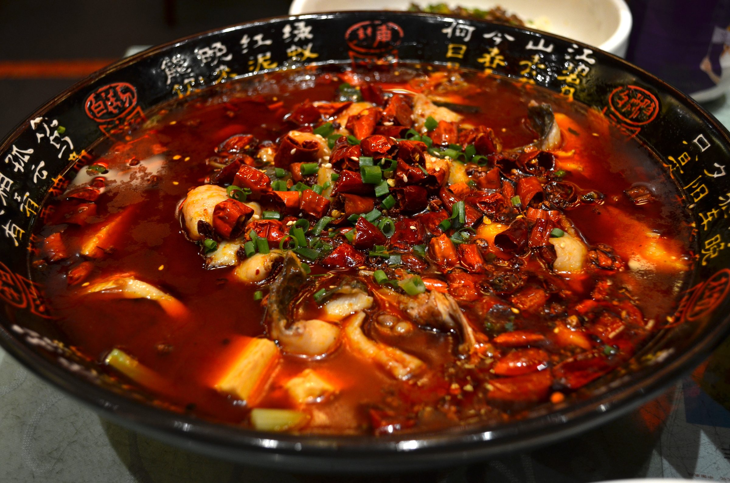 A bowl of authentic Sichuan mapo tofu with soft tofu cubes in bright red chili oil, topped with ground Sichuan peppercorn and minced meat