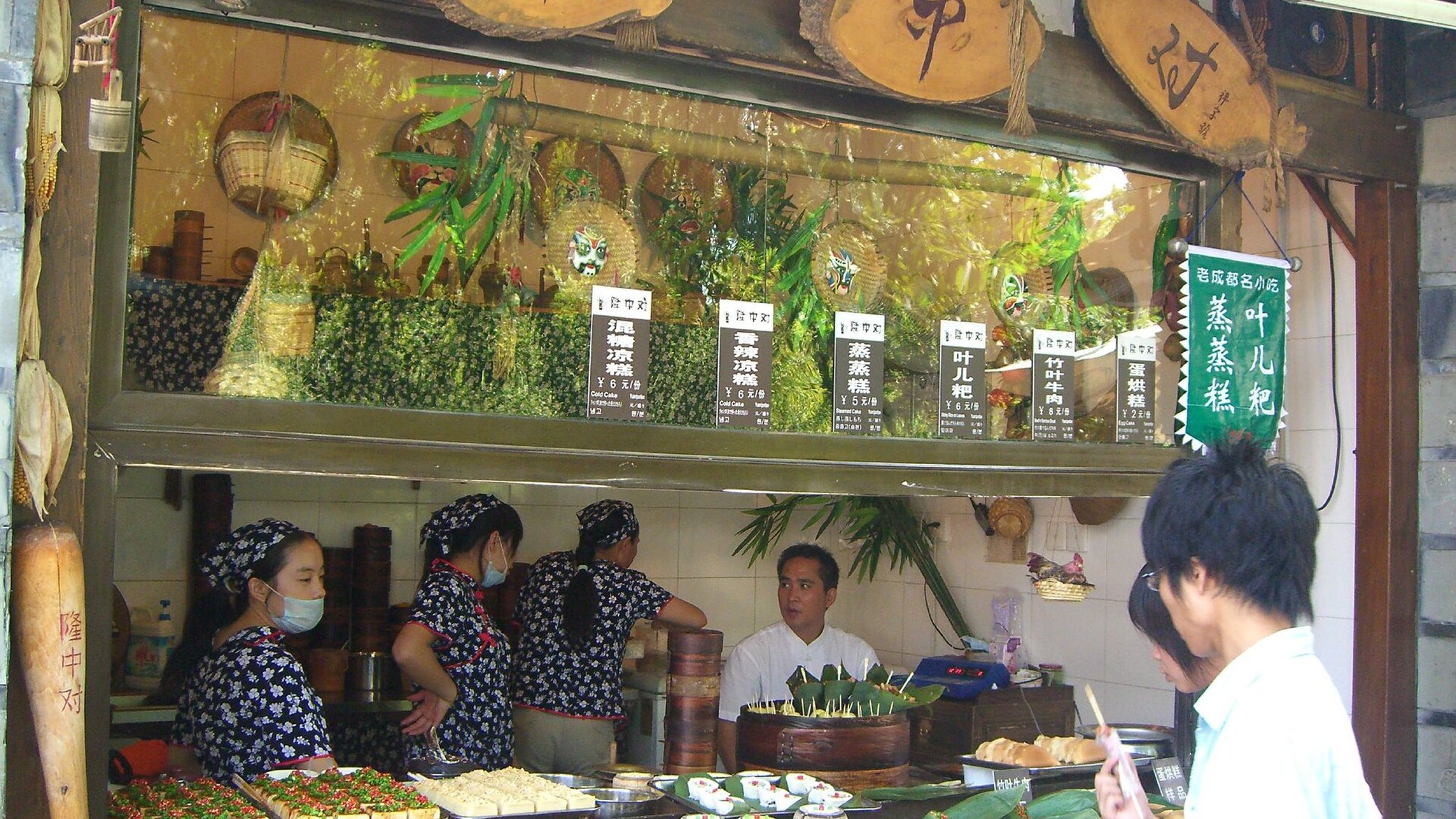 Chengdu snack street vendor with bamboo steamers and traditional Chinese signs showing snack prices in Yuan, with workers in uniform aprons