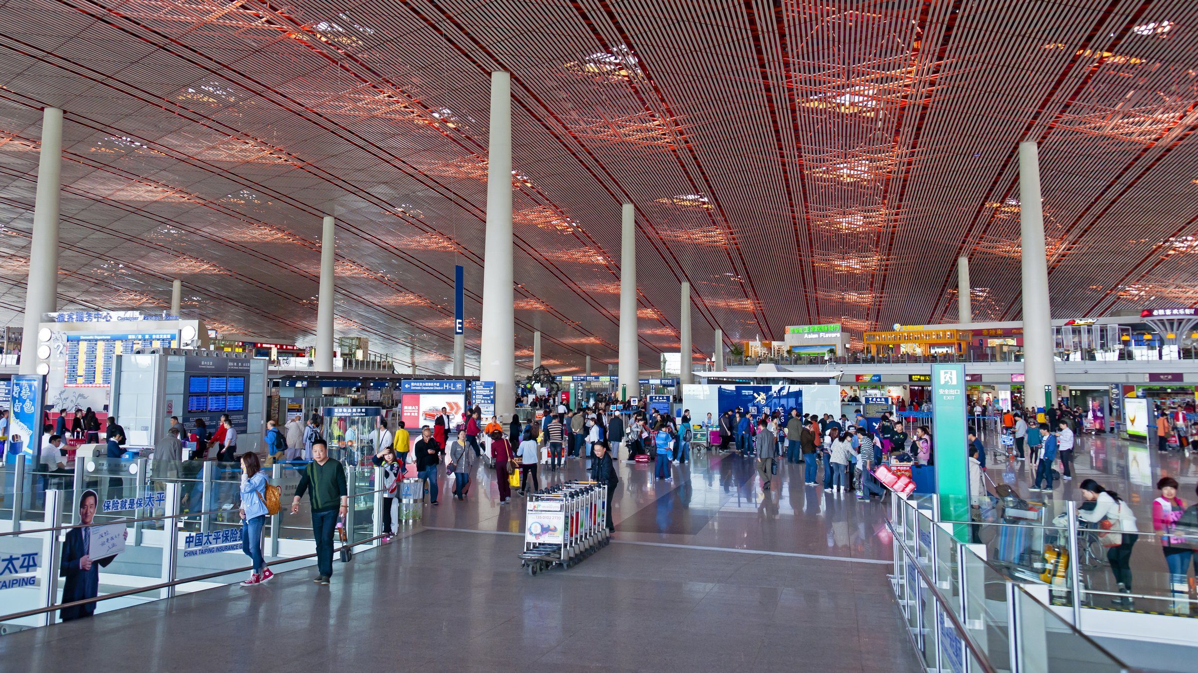 Interior of a modern Chinese airport terminal with Chinese characters on a large information display board and travelers with luggage