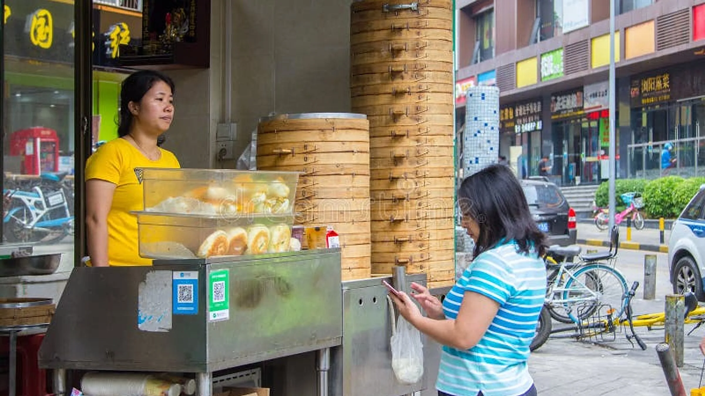 ร้านบ๊ะจ่างริมถนนจีนแท้ๆ เจ้าของร้านแสดง QR code WeChat Pay และ Alipay แบบเคลือบสองใบบนการ์ดที่พิมพ์ พร้อมให้ลูกค้าสแกน ตะกร้าไม้ไผ่ซ้อนอยู่ด้านหลังเคาน์เตอร์