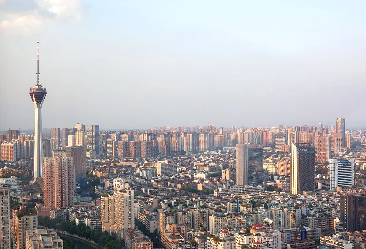 Chengdu skyline in warm afternoon light, with the 339-meter West Pearl Tower (Tianfu Panda Tower) standing out over a dense spread of mid-rise residential blocks.