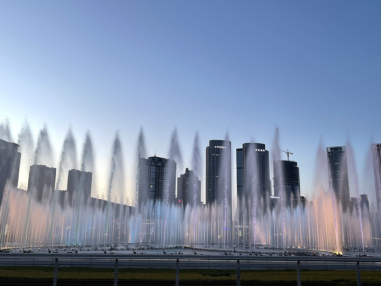 The grand illuminated fountain in Xinghai Square in central Dalian at twilight, with the sea of lights from nearby high-rises in the background.