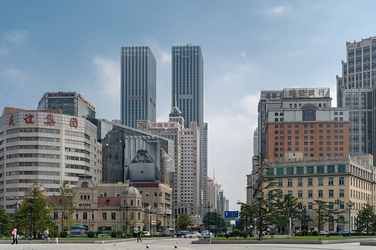 A row of restored 1900s Russian baroque buildings in warm yellow tones along Russian Street in central Dalian, with a stone bridge crossing a small canal in the foreground.