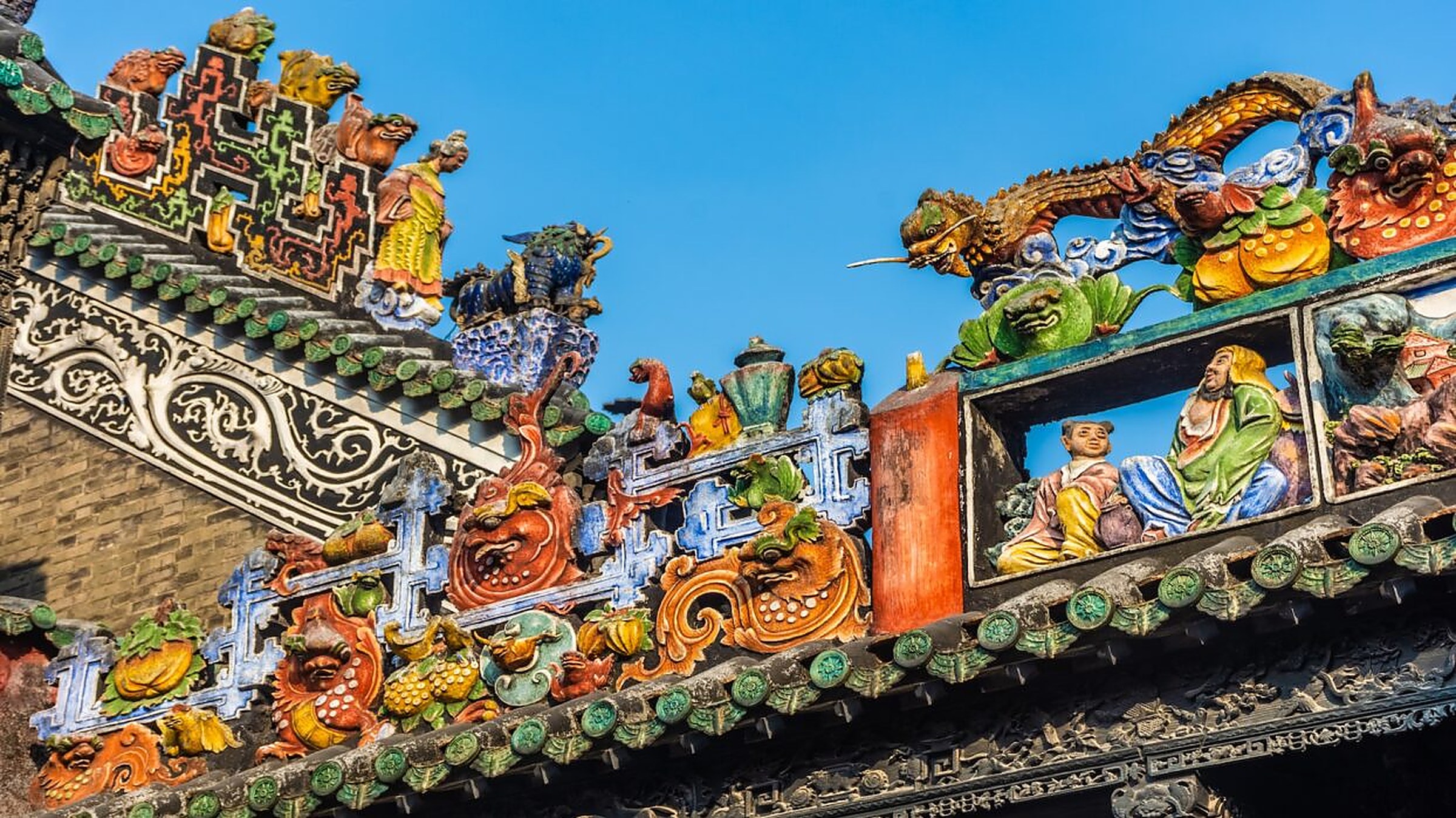 Chen Clan Ancestral Hall — Qing-dynasty ceramic and stone roof sculptures in green, yellow, and white, on the corner of a traditional Lingnan-style building