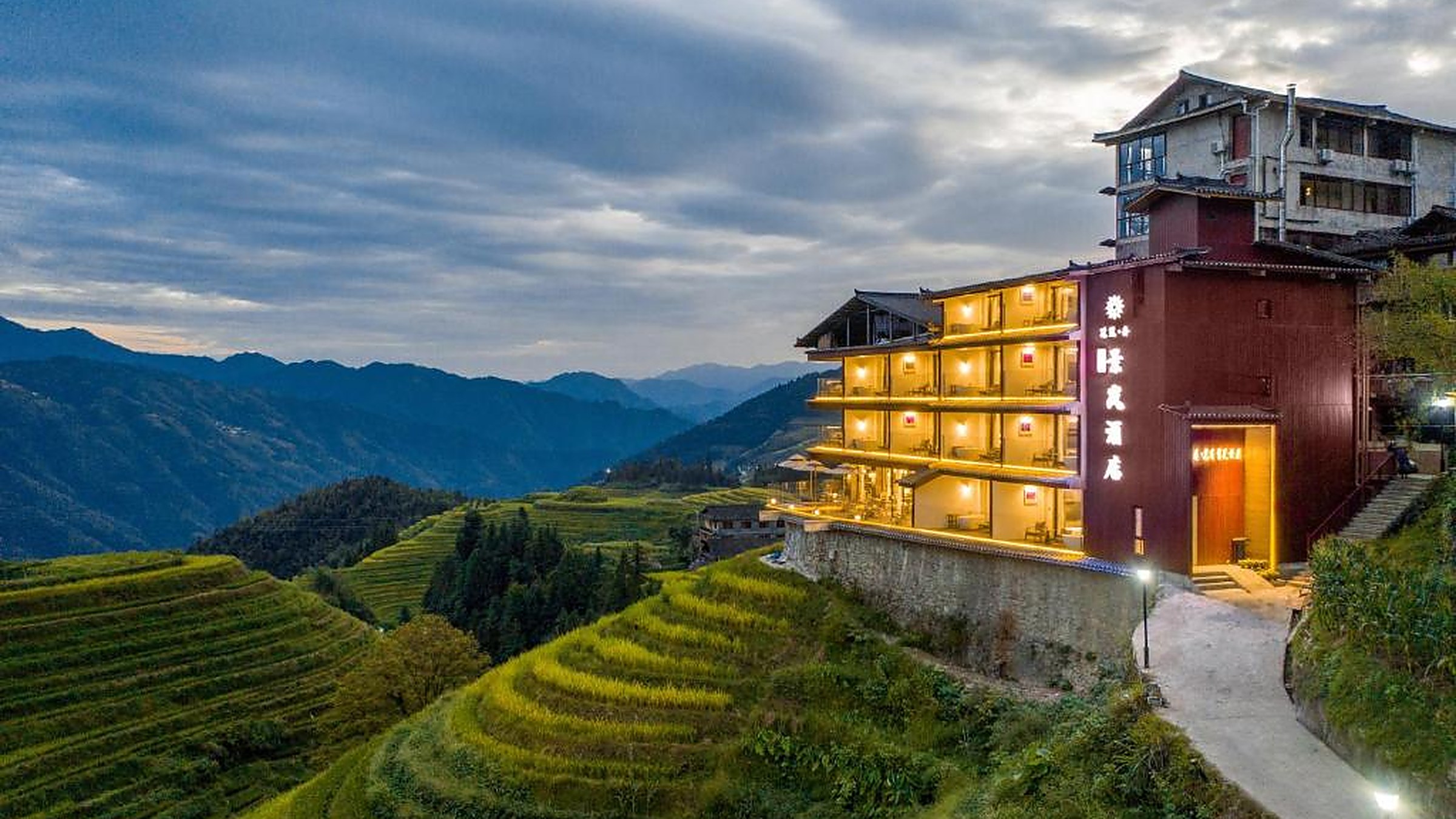 Longji Rice Terraces at sunset — water-filled paddies mirror the orange sky, with wooden Zhuang village rooftops in the foreground