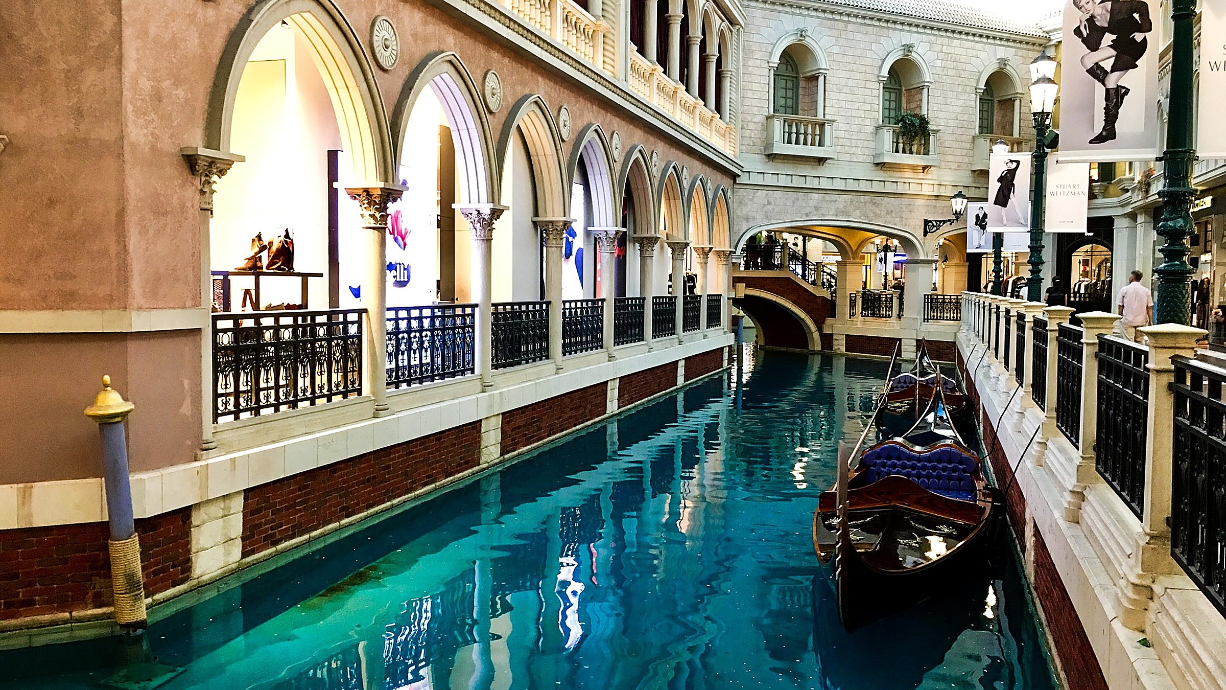 The indoor canal at The Venetian Macao with a gondola passing under a stone bridge, the painted sky ceiling and pastel Venetian-style buildings lining the canal