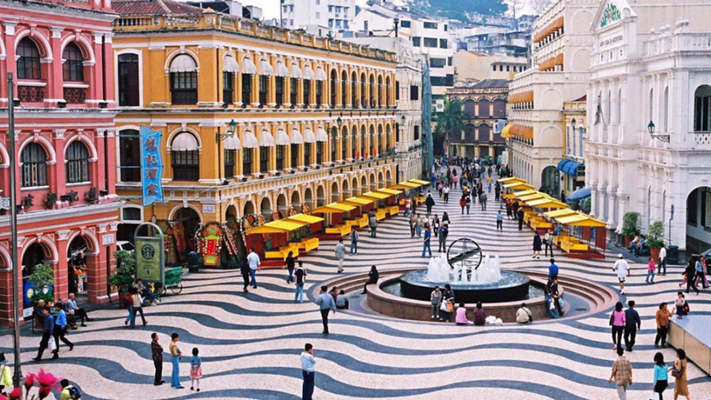 Senado Square in Macau with its distinctive wavy black-and-white cobblestone pavement, surrounded by pastel colonial buildings in yellow, pink, and green