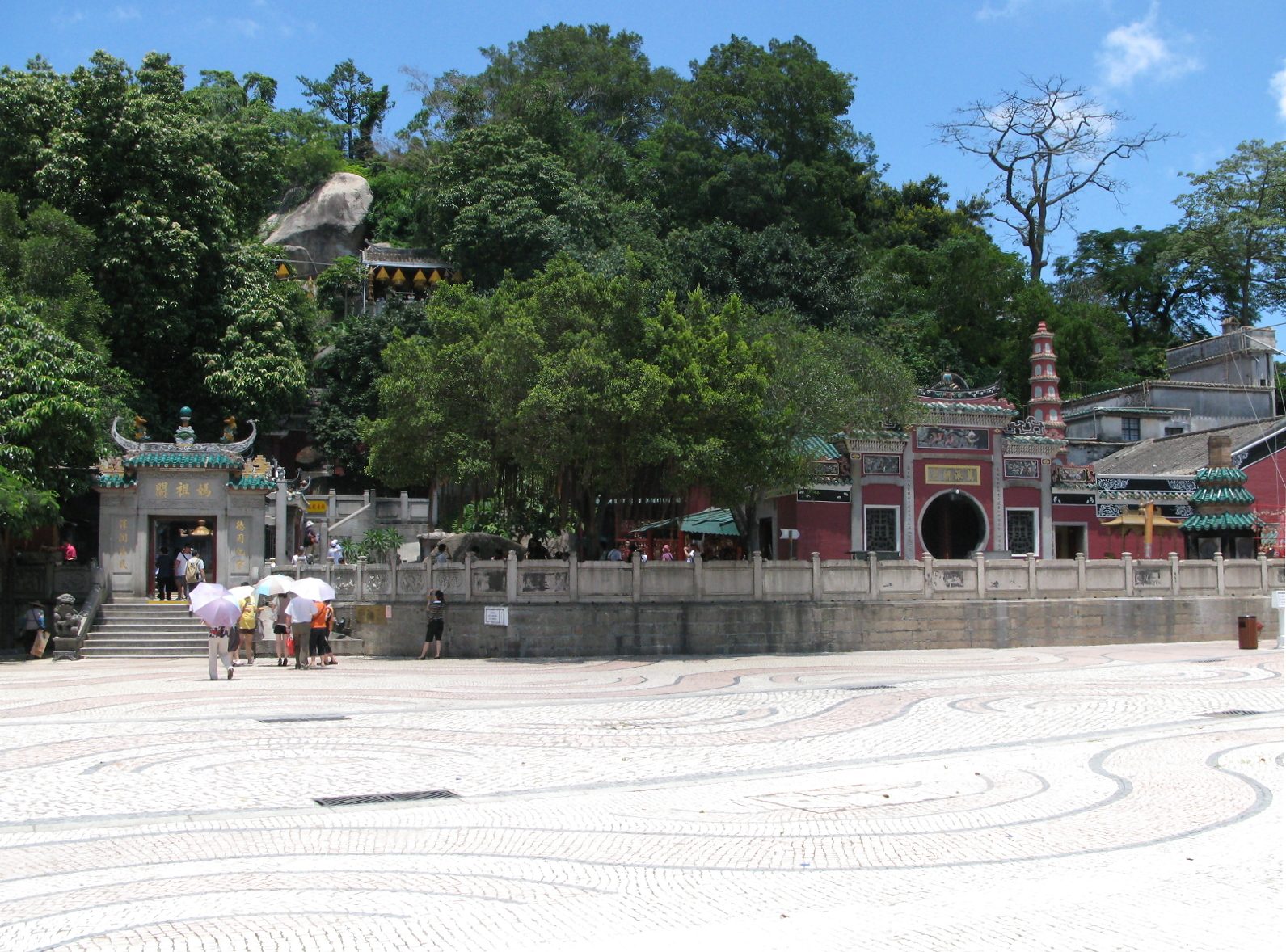 The entrance to A-Ma Temple in Macau, with red Chinese lanterns, incense coils hanging from the eaves, and a 500-year-old stone gateway with carved Taoist guardian figures