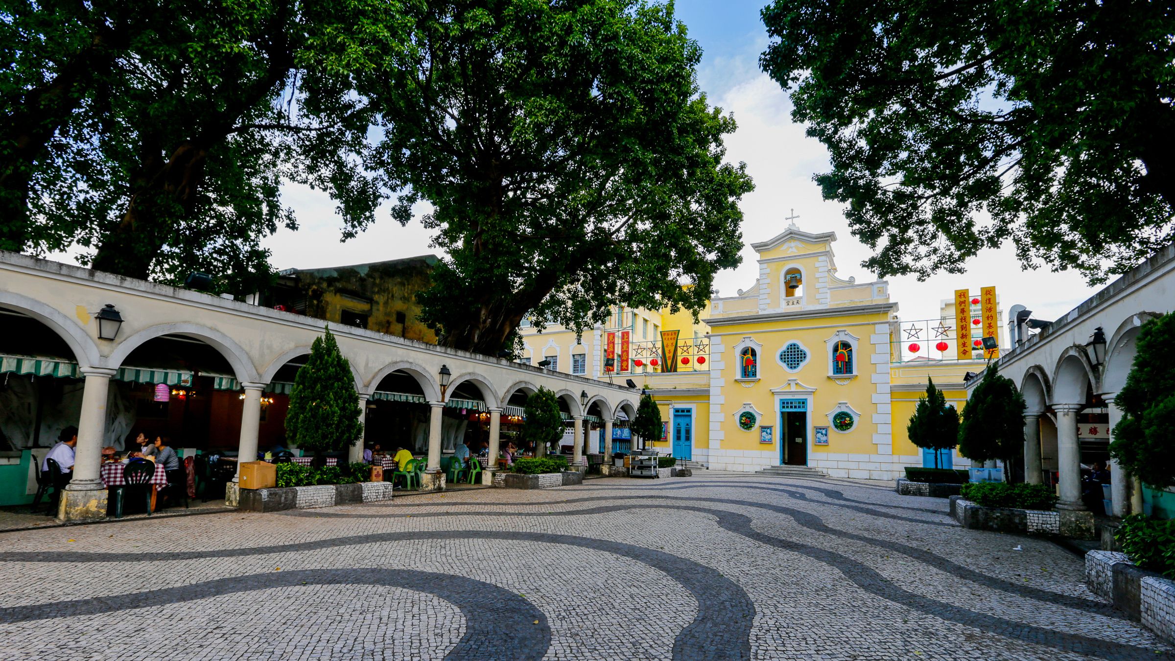 The yellow-painted St. Francis Xavier Chapel in Coloane Village, with a white facade, a small bell tower, and a 17th-century stone wall enclosing the courtyard