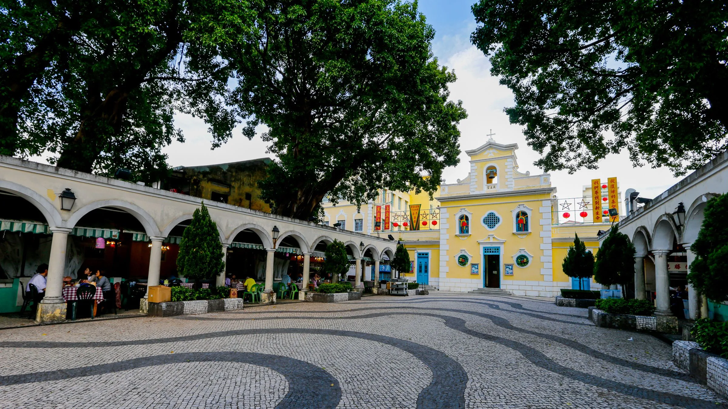 The yellow-painted St. Francis Xavier Chapel in Coloane Village, with a white facade, a small bell tower, and a 17th-century stone wall enclosing the courtyard